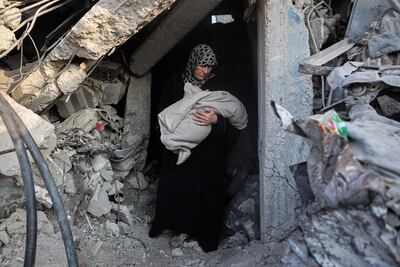 A Palestinian woman carries a baby in the rubble of Jabalia, northern Gaza. AFP