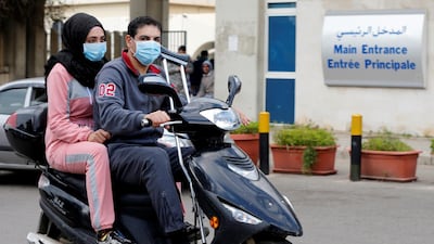 People wearing face masks ride on a motorbike outside Rafik Hariri hospital, where Lebanon's first coronavirus case is being quarantined, in Beirut, Lebanon. REUTERS