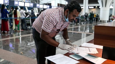 A man wearing latex gloves and a mask, due to the coronavirus pandemic, checks airline tickets and travel documents while behind him Indian nationals residing in Oman queue with their luggage in Muscat International Airport ahead of their repatriation flight from the Omani capital, on May 12, 2020. AFP