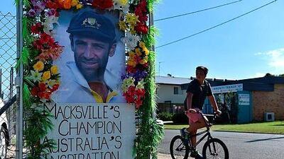 A boy rides his bicycle next to a portrait of the late Australian crciket player Phillip Hughes in his hometown Macksville, some 500 kilometers from Sydney on November 29, 2014. The first Test match between Australia and India was postponed following the death of batsman Phillip Hughes, with a shattered skipper Michael Clarke admitting the team were in "deep pain". AFP PHOTO/ SAEED KHAN