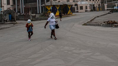 A woman and child cover their heads and faces as they walk across a road in Kingstown strewn with fine ash. AP Photo