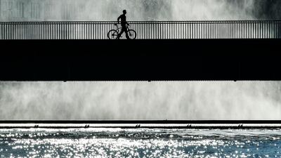 A man walks with his bicycle in the winter sun on a weir over the Ruhr river at Lake Baldeney in Essen, Germany. AP Photo