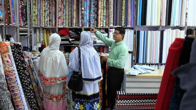 Narendra Devnani helps his customers pick up the right fabric at his textile shop, Champion Textiles, in Satwa in Dubai. Delores Johnson / The National