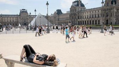 A tourist rests on a bench in front of the Louvre. AFP