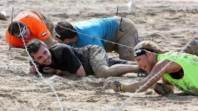 A man smiles as a he encourages a female competitor under the barbed wire.