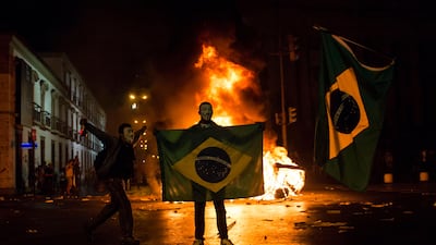 A demonstrator holds a Brazilian flag in front of a burning barricade during the protest. AP Photo / Felipe Dana