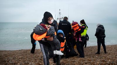 A migrant carries her children ashore at a beach in Dungeness, on the south-east coast of England, on November 24, 2021, after being rescued while crossing the English Channel. AFP