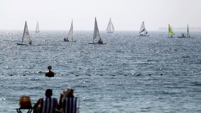 People sit on the beach and watch sailing boats in Dubai. Chris Whiteoak / The National