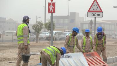 Road workers carry a barrier which was dragged by strong winds in the Musaffah area of Abu Dhabi. Victor Besa / The National