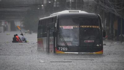 People paddle a boat past a half-submerged passenger bus along a flooded street in Manila. AFP