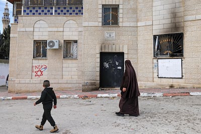 Palestinians walk past Hebrew graffiti on the walls of a house damaged in an attack by Israeli settlers in Jalud, south of Nablus in the occupied West Bank, on March 22, 2026. AFP