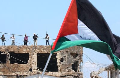 A Palestinian flag is waved during a rally to protest the Israeli incursion into Gaza, as armed Palestinian militants stand guard in the Burj Al Barajneh refugee camp on June 30, 2006. Jean Haddad / AP