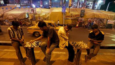 Men play chess on the pavement beside a busy street.