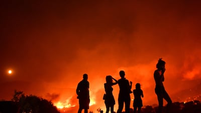 Residents look at flames as a wildfire rages near Palaia Fokaia, about 45 Km south of Athens. AFP