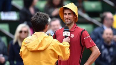 Novak Djokovic, right, wears a yellow rain hat as he is interviewed by former French tennis player Fabrice Santoro after winning his men's fourth round match against Spain's Roberto Bautista at the French Open. Philippe Lopez / AFP
