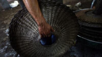 A worker prepares crushed olives between metal plates at a traditional stone press.
