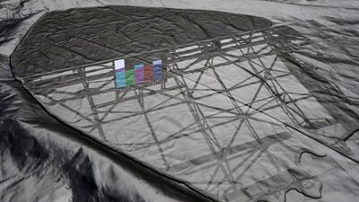 Arthur Ashe Stadium's not-yet-completed roof and a video screen test pattern are reflected in a puddle on the stadium's tarp-covered court after play was postponed by rain on Thursday. Kathy Willens / AP