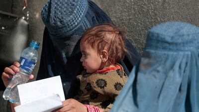 A displaced Afghan woman holds her child as she waits with other women to receive aid supply outside a UNCHR distribution centre in Kabul, Afghanistan. Reuters