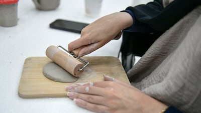 A student uses a rolling pin to make a slab from clay.