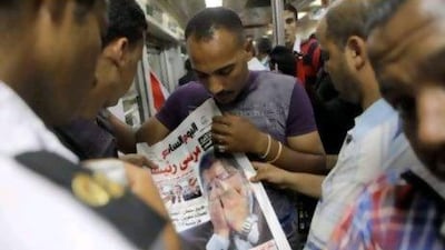 Egyptians read a newspaper featuring their newly elected president Mohammed Morsi in Cairo. Mr Morsi started work on forming a government yesterday even before he had a clear picture of what he could do after the ruling military stripped most of the powers from his post.