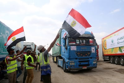 People on the Egyptian side of the Rafah border crossing wave flags as a convoy of lorries carrying humanitarian aid crosses to the Gaza Strip on October 22, 2023. AFP
