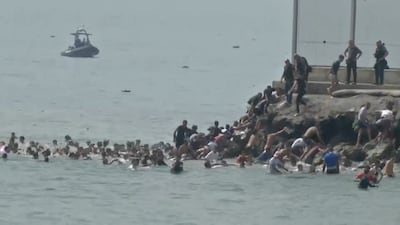 Migrants clamber on to rocks near the border fence in Ceuta. Reuters