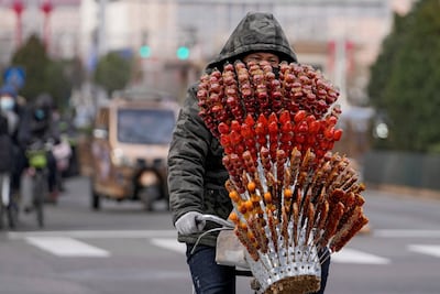 A vendor with a variety of sugar-coated Chinese haw crosses an intersection in Beijing, on January 26. AP