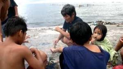 Natividad Villamore cooks mussels on the beach at Manila Bay as children swim in the polluted waters behind her.