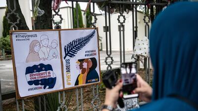 A Muslim woman photographs a poster hung on the fence of Al Noor mosque after it was officially reopened following last week's attack. Getty Images