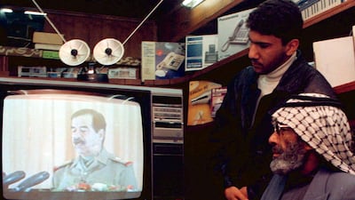 A shopkeeper and his son watch a televised speech by then-Iraqi president Saddam Hussein in January, 1997. Reuters