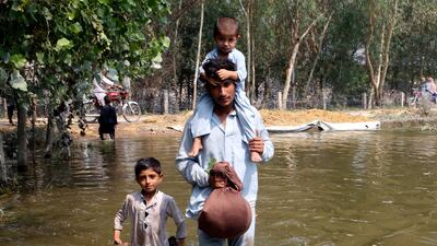 A man and his children wade through floodwaters in Charsadda, Pakistan. AP