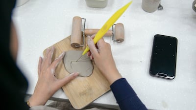 A student uses a sculpting tool to cut out a piece from the clay.
