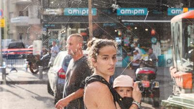 A woman carrying a baby walks past shattered glass in the aftermath of an explosion that took place in Tel Aviv. AFP
