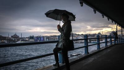 A man waits under the Galata Bridge with Hagia Sophia Mosque and Yeni Mosque in the background on a rainy day. EPA