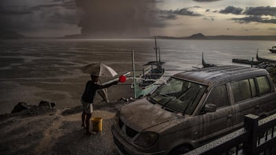 A resident splashes water on a vehicle covered in ash mixed with rainwater as Taal Volcano erupts. Getty Images