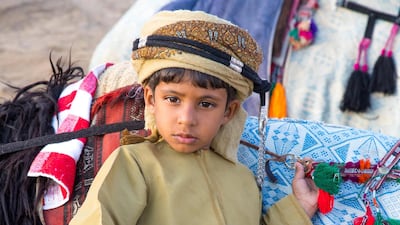 A young Omani boy dressed in traditional clothing posing next to his camel. Camel racing has been added to Unesco's cultural heritage list. Alamy