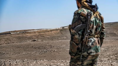 A Syrian Democratic Forces fighter near the town of Al Hol in Hasakah province watches construction work on a concrete border fence being erected on the Iraqi side of the border on March 29, 2022. AFP
