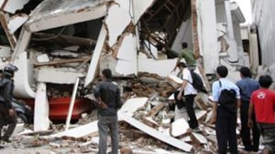 People stand near a collapsed shopping mall after an earthquake hit Padang, on Indonesia's Sumatra island on September 30, 2009.