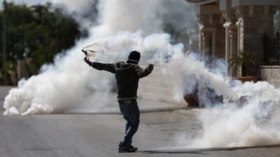 A Palestinian man uses a slingshot to throw back a tear-gas canister towards Israeli soldiers during clashes in the West Bank village of Silwad, north of Ramallah. Thomas Coex / AFP