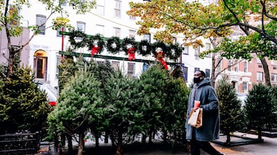 A pedestrian wearing a protective mask passes in front of Christmas trees and wreaths for sale on a sidewalk in New York, U.S. New York City had its credit rating cut by Fitch Ratings because of the impact the coronavirus pandemic is having on the city's economy. Bloomberg