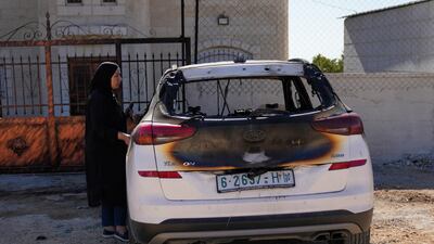 A woman inspects a car burned by Israeli settlers in an attack that left three Palestinians dead in the West Bank. AP