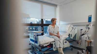 A medium wide-angle view of a woman sitting on the edge of her hospital bed before she goes for some treatment for her breast cancer. Getty Images