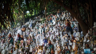 An elderly woman walks past unwanted statues of deities, gathered and repaired after their owners discarded them, on a rocky slope running down to the sea in Hong Kong. Anthony Wallace / AFP
