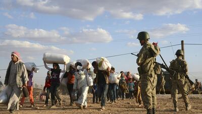 Turkish soldiers stand guard as Syrian refugees gather at the border. AP Photo