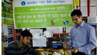 A shopkeeper transfers money for customers using text commands on a mobile phone in New Delhi. Manpreet Romana / AFP