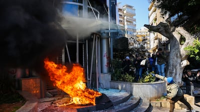 A protester throws a brick at a bank after setting fire to tyres during a demonstration in Beirut on February 16, 2023. Dozens of angry Lebanese demonstrators attacked several banks on February 16 after the local currency dropped in value to a record low in as part of a deepening economic crisis, AFP photographers said. (Photo by Joseph EID / AFP)