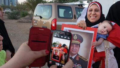 Ganaa holds her baby Yossef in a long line of voters at the Egyptian embassy, while also holding a poster of Abdel Fattah El Sisi. Delores Johnson / The National