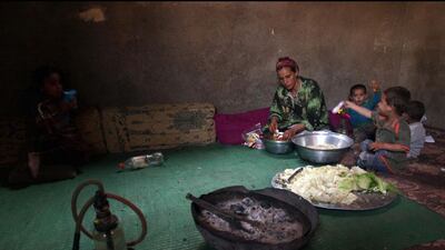 A Palestinian refugee prepares food as her children sit next to her in their house in Gezirat al-Fadel village.