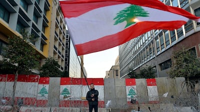 An anti-government protester waves a national flag in front of a concrete wall set up by Lebanese police to block a road leading to the parliament building in downtown Beirut, Lebanon. EPA
