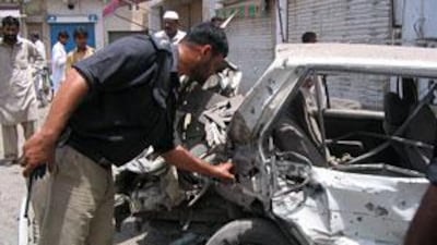 A Pakistani policeman inspects a destroyed car after a bomb blast at a market in Dera Ismail Khan.